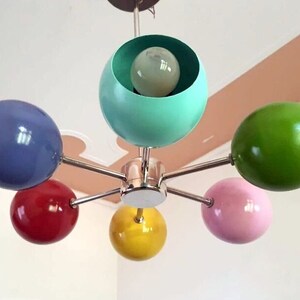 May include: A six-light chandelier with colorful spherical shades. The shades are blue, green, red, yellow, and pink. The chandelier has a chrome finish.