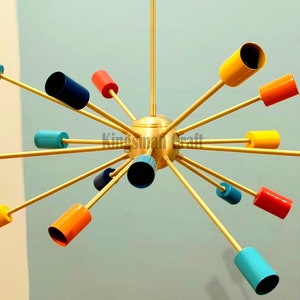 Puede incluir: Una lámpara de araña dorada con múltiples brazos que se extienden hacia afuera. Cada brazo tiene una luminaria cilíndrica de colores. Los colores incluyen rojo, amarillo, azul y turquesa.