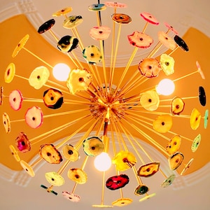 May include: A gold metal chandelier with multiple agate slices in various colours and patterns hanging from it. The chandelier is suspended from a white ceiling.