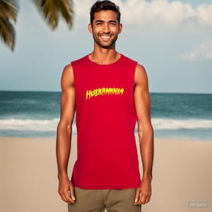 May include: A red sleeveless vest with the yellow text "HULKAMANIA" printed on the front. The vest is made of a soft material. The background shows a beach with the sea and blue sky.