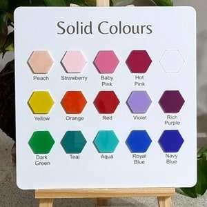 Op de afbeelding: Een wit bord met de tekst "Solid Colours" bovenaan. Het bord is verdeeld in drie rijen met zes zeshoekige kleurstalen. De kleuren zijn perzik, aardbei, babyroze, felroze, geel, oranje, rood, violet, donkerpaars, donkergroen, teal, aqua, koninklijkblauw en marineblauw.