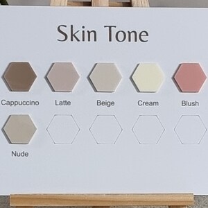 Op de afbeelding: Huidtintkleurenkaart met 8 zeshoekige kleurstalen met de labels: Cappuccino, Latte, Beige, Cr&egrave;me, Blush, Nude.
