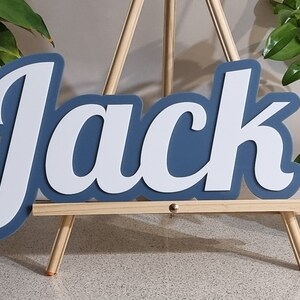 Op de afbeelding: Een blauw en wit houten naambord met de tekst "Jack" op een klein houten ezel.