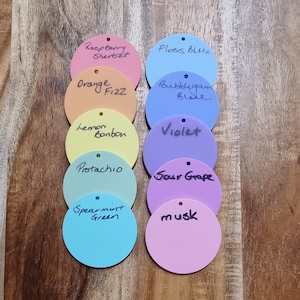 Pode incluir: Uma cole&ccedil;&atilde;o de etiquetas circulares coloridas com r&oacute;tulos manuscritos. As cores incluem rosa, laranja, amarelo, verde, azul e roxo. Cada etiqueta tem um pequeno orif&iacute;cio na parte superior. Os r&oacute;tulos incluem "Raspberry Sherbet", "Orange Fizz" e "Lemon Bonbon".