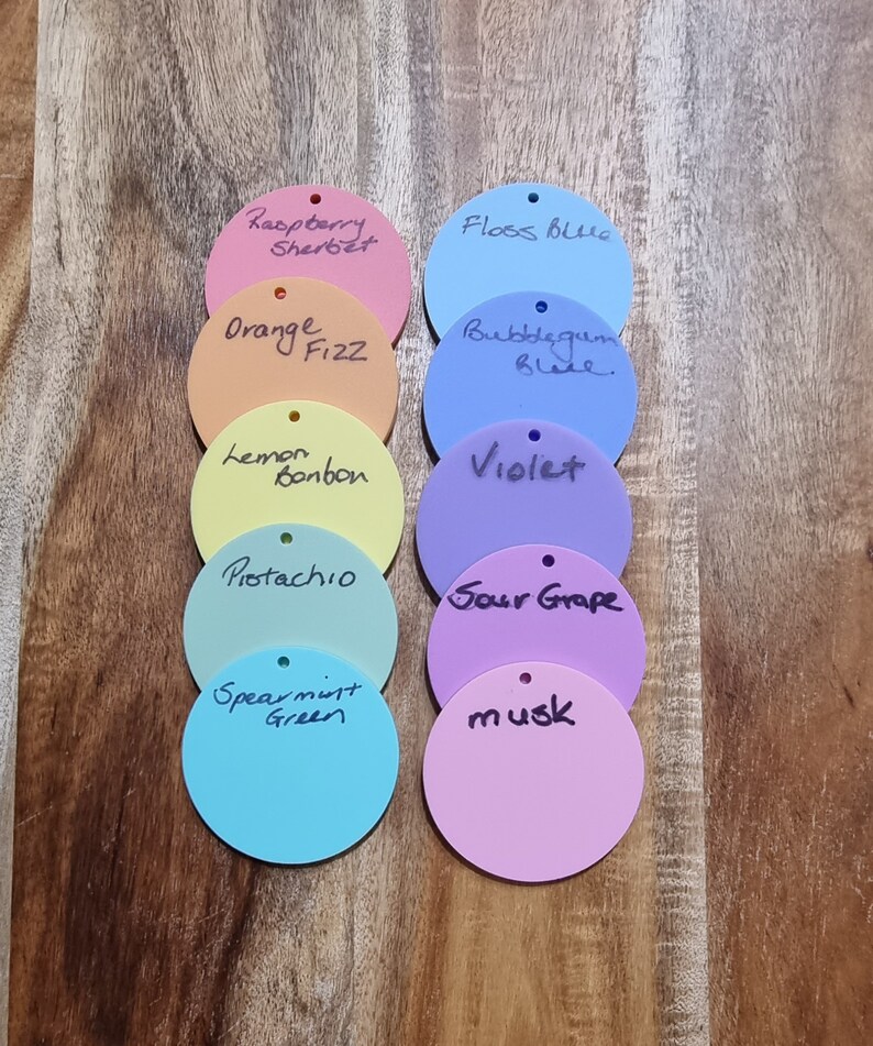 Pode incluir: Uma cole&ccedil;&atilde;o de etiquetas circulares coloridas com r&oacute;tulos manuscritos. As cores incluem rosa, laranja, amarelo, verde, azul e roxo. Cada etiqueta tem um pequeno orif&iacute;cio na parte superior. Os r&oacute;tulos incluem "Raspberry Sherbet", "Orange Fizz" e "Lemon Bonbon".