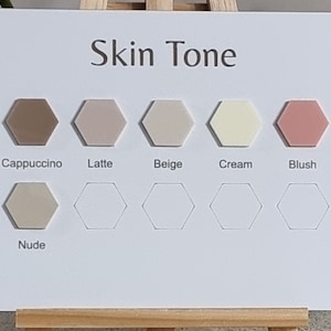 Pode incluir: Um cart&atilde;o branco com o texto "Skin Tone" e uma s&eacute;rie de amostras de cores hexagonais. As amostras exibem tons rotulados como Cappuccino, Latte, Beige, Cream, Blush e Nude. O cart&atilde;o &eacute; apoiado por um pequeno cavalete de madeira.
