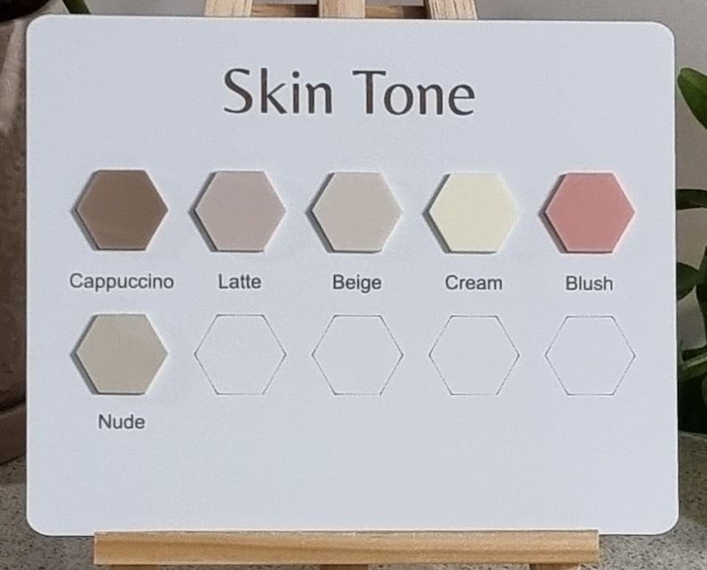 Pode incluir: Um cart&atilde;o branco com o texto "Skin Tone" e uma s&eacute;rie de amostras de cores hexagonais. As amostras exibem tons rotulados como Cappuccino, Latte, Beige, Cream, Blush e Nude. O cart&atilde;o &eacute; apoiado por um pequeno cavalete de madeira.