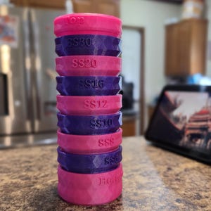May include: A vertical stack of nine cylindrical plastic sorting rings alternating between bright pink and dark purple. Each ring features a faceted geometric exterior and is embossed with text including Top, SS30, SS20, SS16, SS12, SS10, SS8, SS6, and Bottom.