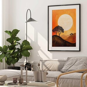 May include: A framed print of a sunset landscape with two trees silhouetted against a large, white sun. The sky is a gradient of orange, yellow, and red. The hills are a dark brown.