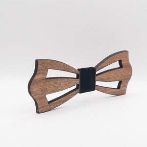 May include: A wooden bow tie with a unique design. The bow tie is made of brown wood with a black center band. The design features cut-out sections, adding a modern touch to the classic accessory. Perfect for formal events or adding flair to an outfit.