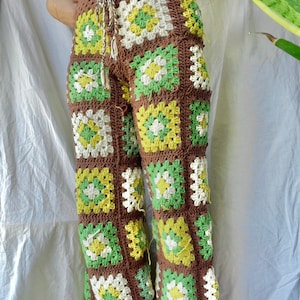May include: Brown crochet pants with green, yellow, and white squares. The pants have fringe at the bottom.