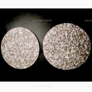 May include: Two round white mother of pearl coasters with a geometric pattern. The coasters are approximately 10 inches in diameter.