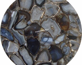 May include: A round, gray and brown agate stone table top. The table top is made of many small pieces of agate that have been cut and polished. The agate is a natural stone with a variety of colors and patterns. The table top is perfect for a coffee table or end table.