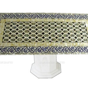 May include: A white marble table with a decorative inlay of mother of pearl and blue floral designs. The table has a square top and a single pedestal base.