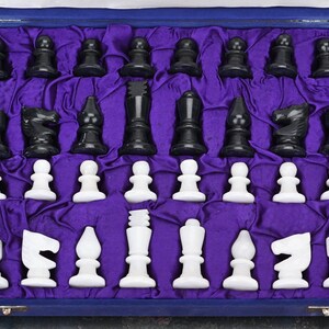 May include: A set of black and white chess pieces in a purple velvet lined box. The pieces are made of polished stone and are arranged in their starting positions.