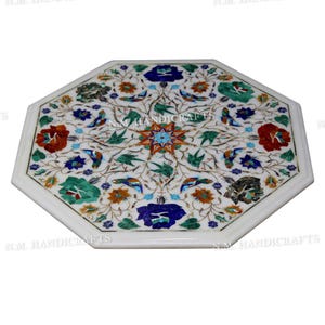 May include: Octagonal white marble table top with intricate floral and bird designs inlaid with colourful semi-precious stones. The table top is approximately 50 cm in diameter.