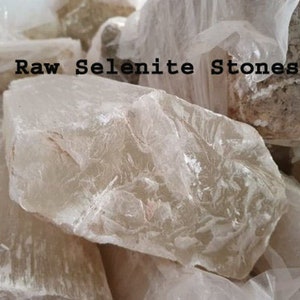 May include: A close-up of a pile of raw selenite stones. The stones are a translucent white with a slight shimmer. The text "Raw Selenite Stones" is visible in the image.