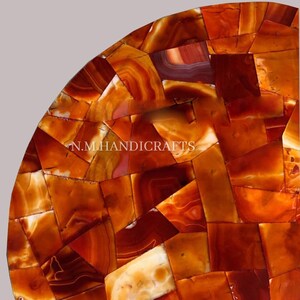 May include: A half-circle table top made of orange, red, and white agate stone. The table top is made of many small pieces of agate that are arranged in a mosaic pattern. The table top is polished and has a smooth surface.