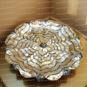 May include: A decorative, handcrafted bowl with a floral design. The bowl is made of iridescent mother-of-pearl pieces, arranged in a petal pattern. It sits on a gold-coloured surface, adding a touch of elegance.