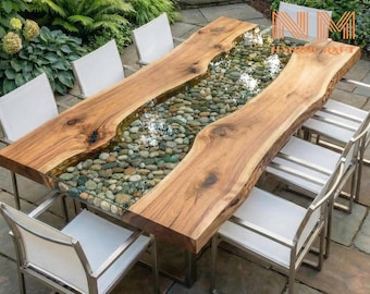 May include: A rectangular dining table featuring two natural live-edge wood slabs separated by a central glass-topped channel filled with smooth, multi-colored river stones, surrounded by six chairs with white fabric seats and metal frames.