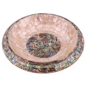 May include: A round, white, mother-of-pearl bowl with a decorative iridescent abalone shell inlay. The bowl has a scalloped edge and is perfect for serving snacks or holding jewellery.