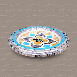 May include: A round decorative tray with a mosaic design. It has a turquoise border and a central floral pattern with an elephant motif. The tray is made of mother-of-pearl and other materials.