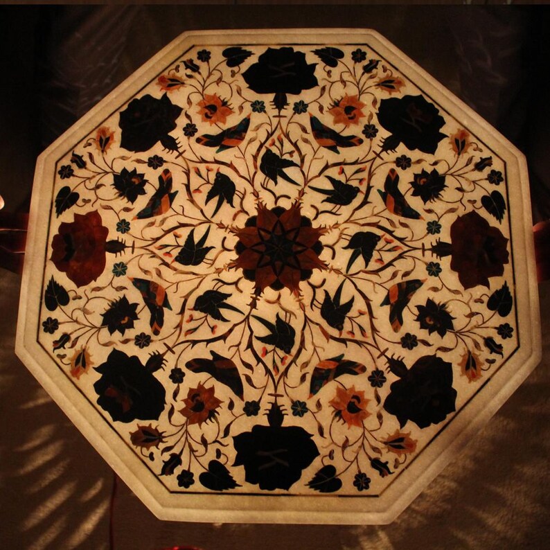 May include: Octagonal table top featuring an intricate floral design inlaid with various coloured stones. The design incorporates birds, flowers, and leaves in shades of black, white, brown, red, and green.