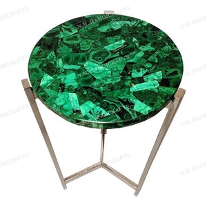 May include: A round green malachite mosaic table top with a silver metal base. The table top is made of many small pieces of malachite, each with a unique pattern. The base is made of three legs that meet in the center.