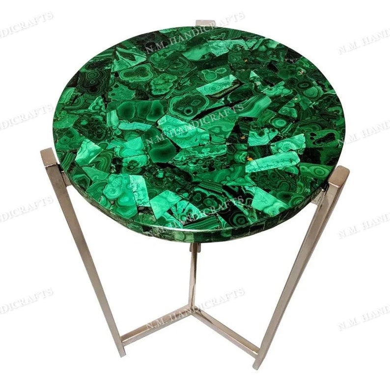 May include: A round green malachite mosaic table top with a silver metal base. The table top is made of many small pieces of malachite, each with a unique pattern. The base is made of three legs that meet in the center.