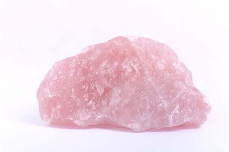 May include: A large, rough, pink rose quartz crystal. The crystal has a natural, unpolished surface.
