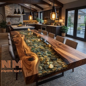 May include: A large, custom-made dining table with a live-edge wooden top. The center of the table is filled with smooth river stones encased in clear resin. The table is surrounded by gray upholstered chairs and is in a modern kitchen setting.