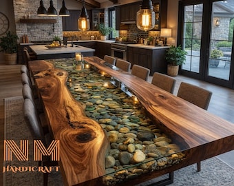 May include: A large rectangular dining table featuring two thick live-edge wood slabs with a central glass-topped channel filled with smooth, multi-colored river stones. The table is supported by a black metal frame and includes gray upholstered chairs.