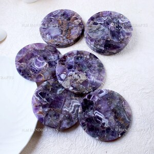 May include: Set of six round amethyst coasters. Each coaster is made of natural amethyst stone and features a unique purple and white pattern. The coasters are ideal for protecting your furniture from scratches and spills.