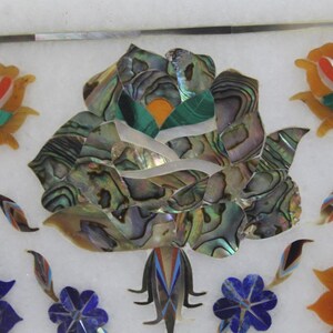 May include: A white marble inlay featuring a large rose crafted from iridescent mother of pearl, surrounded by smaller flowers in shades of blue, green, and orange.
