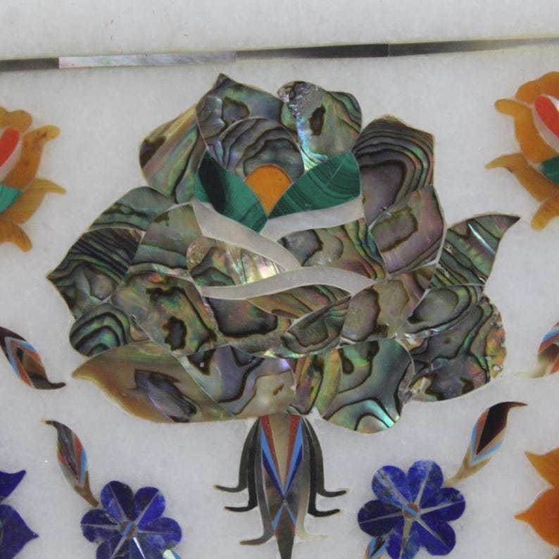 May include: A white marble inlay featuring a large rose crafted from iridescent mother of pearl, surrounded by smaller flowers in shades of blue, green, and orange.