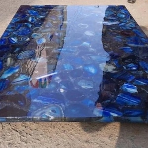 Könnte beinhalten: Eine blaue Achat-Tischplatte mit Hochglanz-Finish. Die Tischplatte besteht aus vielen Achat-Stücken, die geschnitten und poliert wurden, um ein einzigartiges und wunderschönes Design zu schaffen.