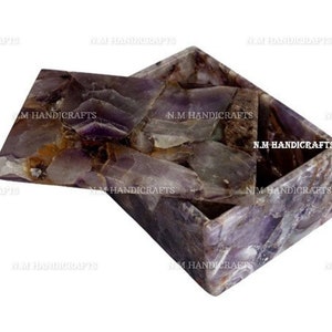 May include: A rectangular amethyst gemstone box with a hinged lid. The box is made of natural amethyst crystals that have been polished and cut into a smooth surface. The box is a beautiful and unique piece of jewelry storage or decorative object.