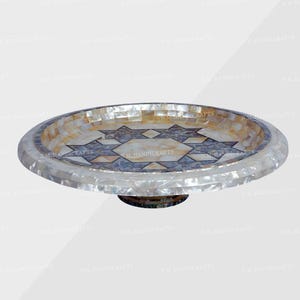May include: A decorative, handcrafted serving tray with a raised pedestal base. The tray features a mosaic design with a star pattern in shades of blue, beige, and white. The outer rim is inlaid with mother-of-pearl.