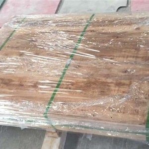 May include: A pallet of wooden planks wrapped in clear plastic. The planks have a natural wood grain appearance and are secured with green straps. The plastic wrap is tightly sealed.
