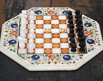 Può includere: Una scacchiera in marmo bianco con pezzi degli scacchi bianchi e neri. La scacchiera è decorata con motivi floreali blu, arancio e verdi. La scacchiera è ottagonale e ha un bordo in marmo bianco.