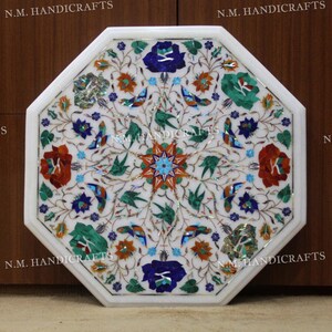 May include: Octagonal white marble table top with an intricate floral design inlaid with colourful stones, including red, blue, green, and gold. The table top is surrounded by a white border.