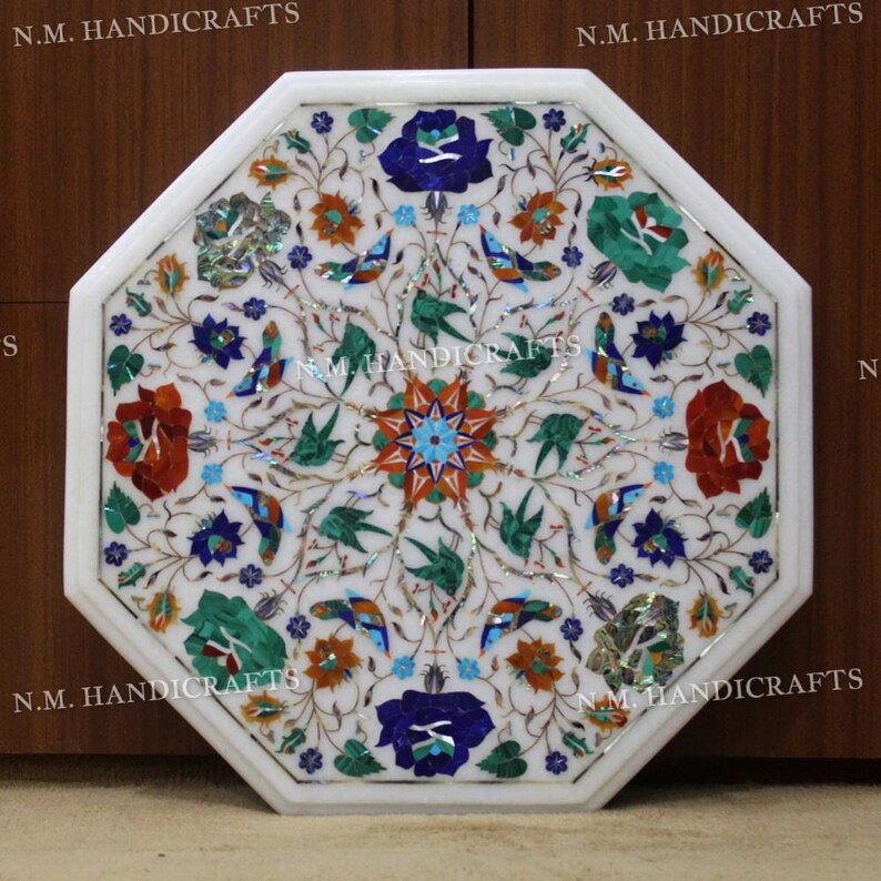 May include: Octagonal white marble table top with an intricate floral design inlaid with colourful stones, including red, blue, green, and gold. The table top is surrounded by a white border.