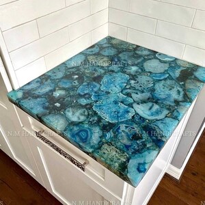 Può includere: Primo piano di un piano di lavoro in agata blu con uno schienale in piastrelle bianche. Il piano di lavoro è in pietra naturale e presenta un motivo unico di blu, verde e bianco.