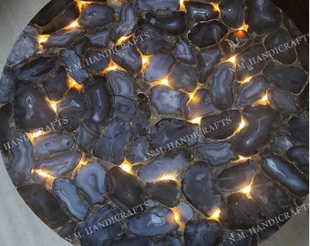 May include: A round table top made of agate slices with a black and white pattern. The agate slices are illuminated from below, creating a warm glow. The table top is approximately 30 inches in diameter.