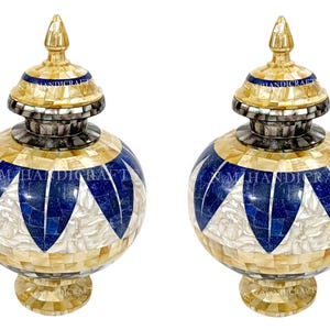 May include: Two decorative urns with a mosaic design. The urns feature a spherical body with a pattern of blue, white, and gold tiles. Each urn has a matching lid and base, with a gold finial on top. The urns are set against a white background.