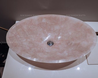 May include: A large, oval-shaped, pink onyx sink with a drain hole in the center. The sink is made of natural stone and has a unique, marbled pattern.
