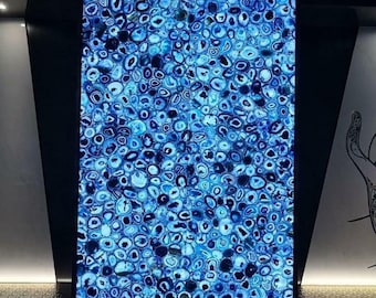 May include: A close-up of a blue agate wall panel with a black frame. The panel is made up of many small, round agate slices, each with a unique pattern. The agate is a natural stone with a variety of colors, including blue, green, and white. The panel is illuminated from behind, creating a beautiful, shimmering effect. N.M. Handicrafts is printed at the bottom of the image.