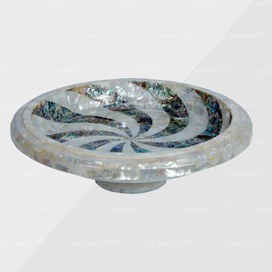 May include: Oval decorative bowl with a mosaic design. The bowl features a white mother-of-pearl exterior with a swirling pattern of iridescent abalone shell in the center. The bowl is raised on a small, circular base.