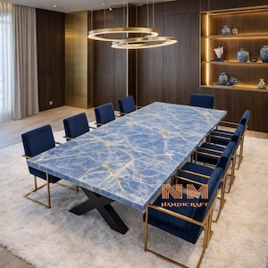 Puede incluir: Una mesa de comedor rectangular con una superficie de mármol azul con vetas blancas y una base negra en forma de X, rodeada de ocho sillas de terciopelo azul marino con marcos de metal dorado. El texto NM HANDICRAFT se ve en la mesa.