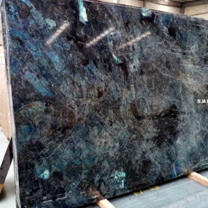 Könnte beinhalten: Eine große Platte aus blauem und schwarzem Granit mit einem wirbelnden Muster. Der Granit ist poliert und hat eine glänzende Oberfläche. Die Platte liegt auf Holzstützen. Der Text "N.J.M HANDICRAFTS" ist in der unteren rechten Ecke des Bildes sichtbar.